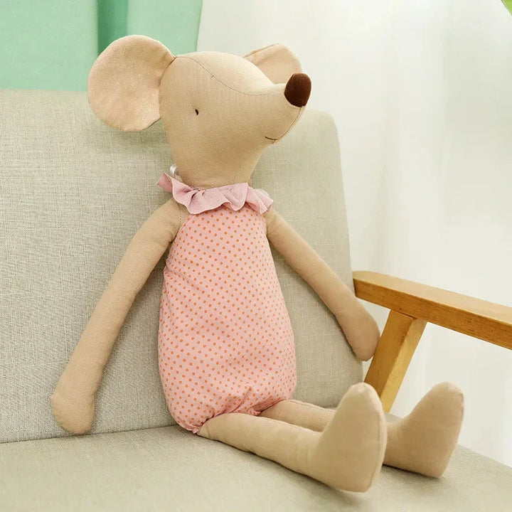 Stuffed mouse toy in a pink dress sitting on a light-colored couch.