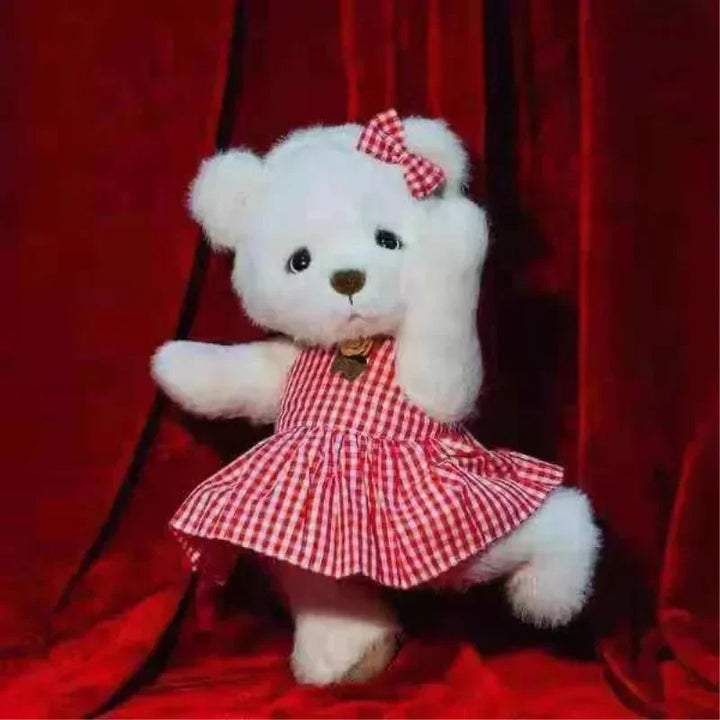 White teddy bear wearing a red checkered dress and bow against a red background.