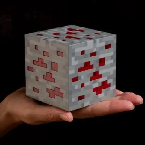 Block-like object with red and gray pattern held in hands against a black background.