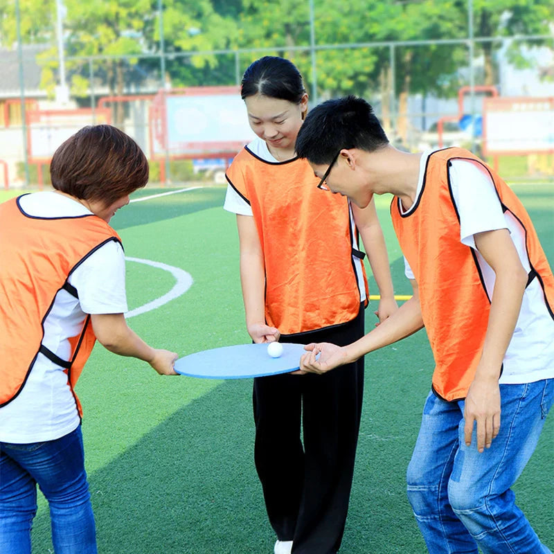 Three people in orange vests holding a blue frisbee on a sports field.
