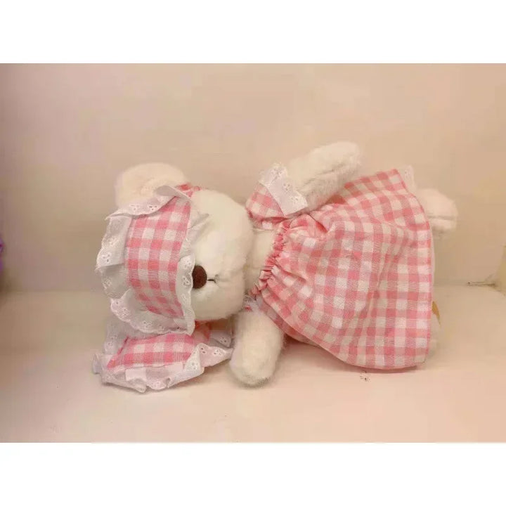 Plush toy bear wearing a pink checkered dress on a light background.