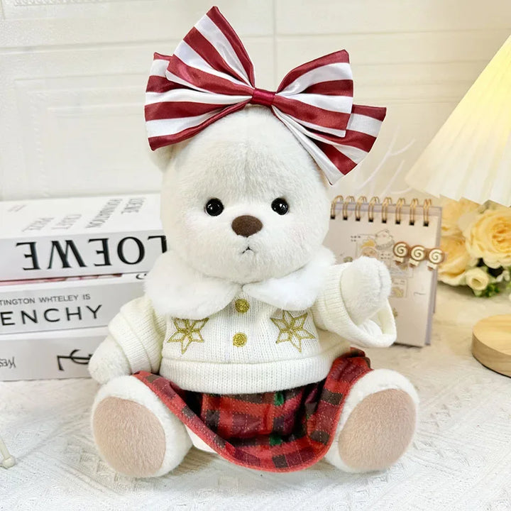White teddy bear with a red and white striped bow, sweater, and plaid skirt on a light background.