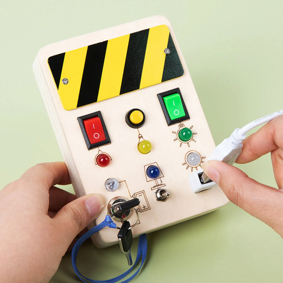 Children's toy control panel with colorful buttons and a hand holding a cable on a light green background.