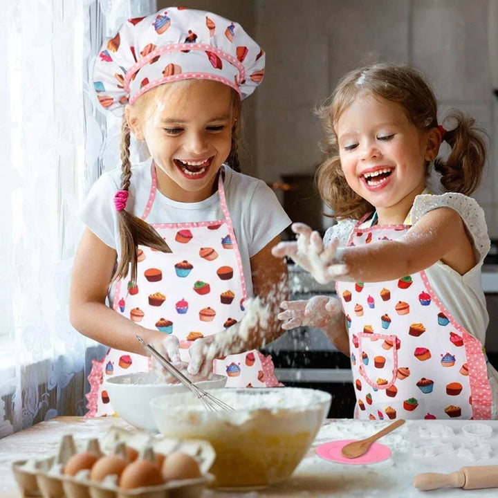Two young girls in a kitchen, wearing aprons and playing with flour.