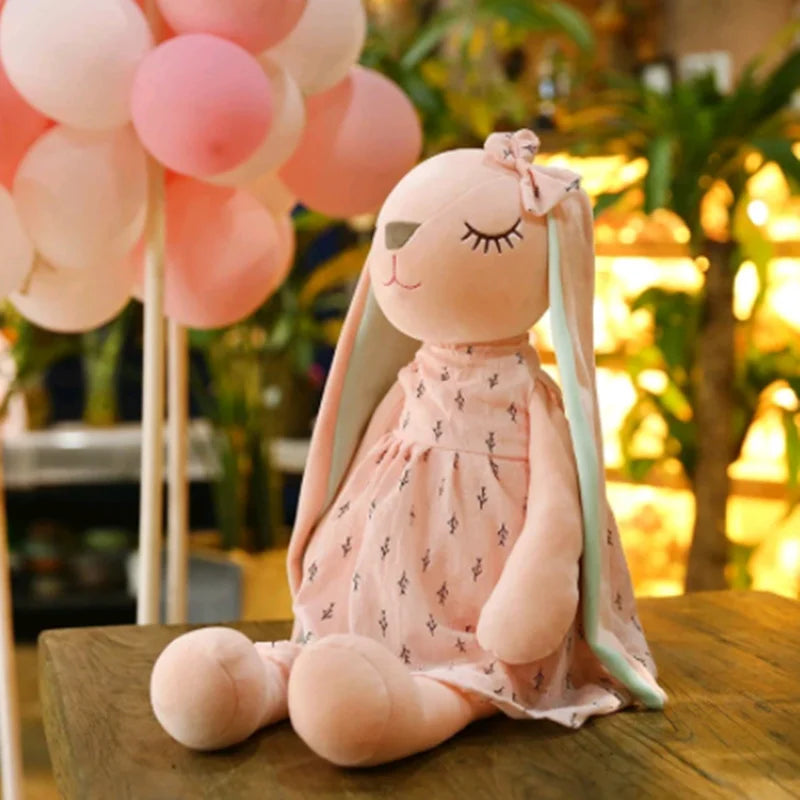 Plush rabbit toy in a dress with pink balloons in the background.
