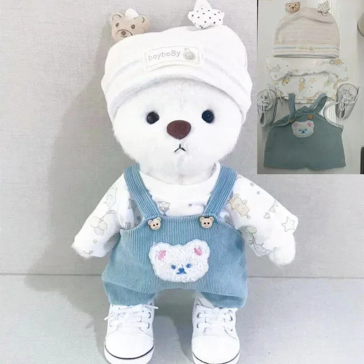 White teddy bear wearing a blue outfit with bear design, white shoes, and a matching hat on a light gray background.