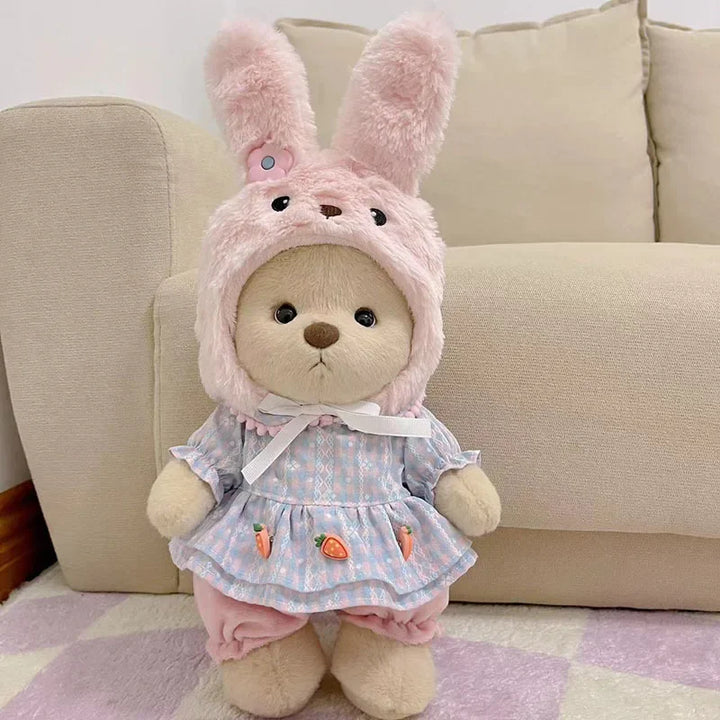 Teddy bear wearing a pink bunny costume with a checkered dress on a couch.
