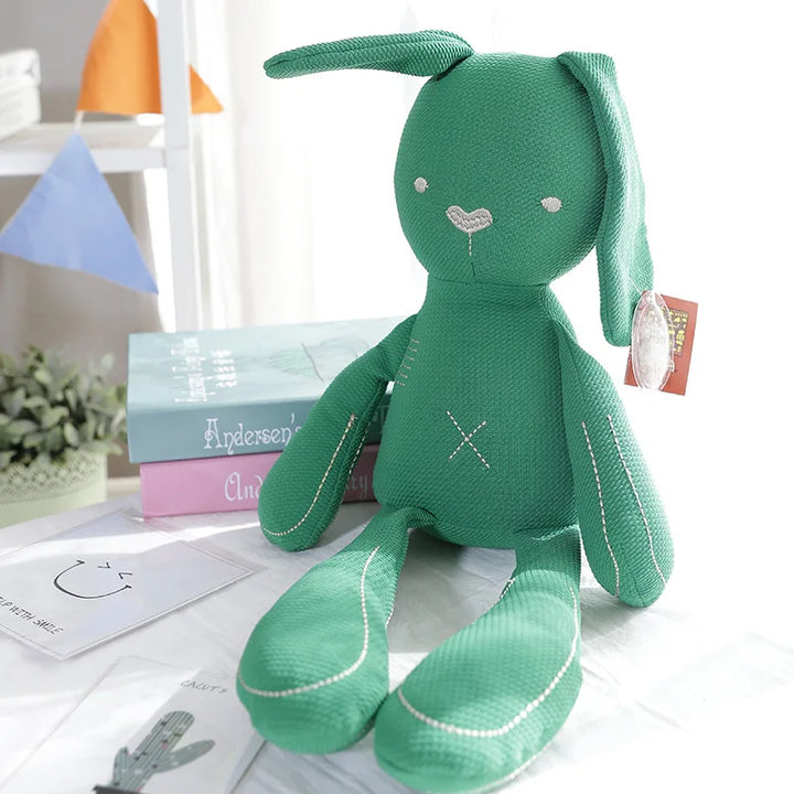 Green plush toy with bunny ears on a white surface with books and decorative items in the background.