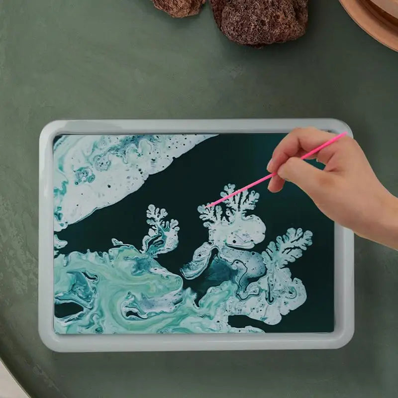 Hand holding a pink straw over a tablet displaying an underwater scene with marine life on a green surface.