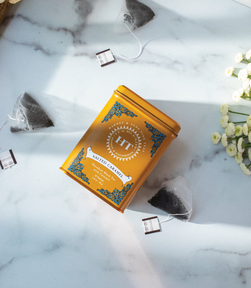 Orange tea box with HT branding on a marble surface with tea bags and flowers.