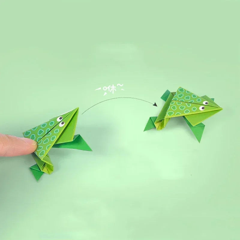Two origami frogs on a green background.