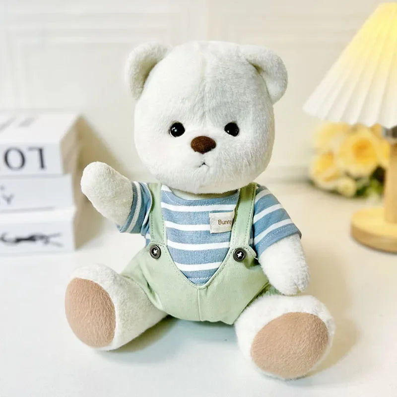 White teddy bear with a striped shirt and green overalls on a light background.