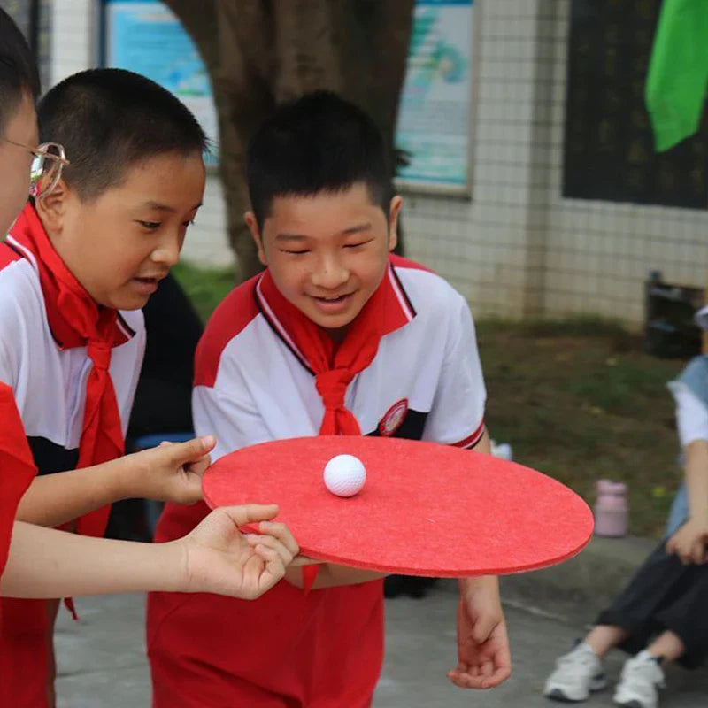Children playing with a red paddle and white ball outdoors.