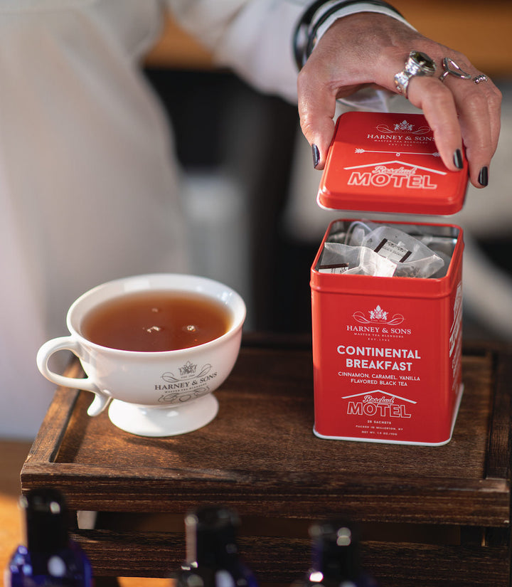 Red tea tin labeled Continental Breakfast with a cup of tea on a wooden surface.