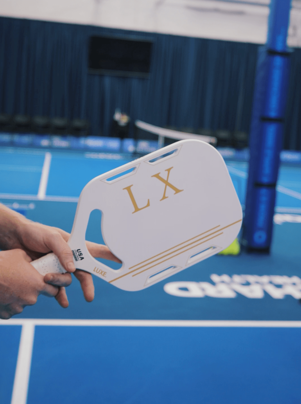Person holding a paddle with LX branding on a badminton court