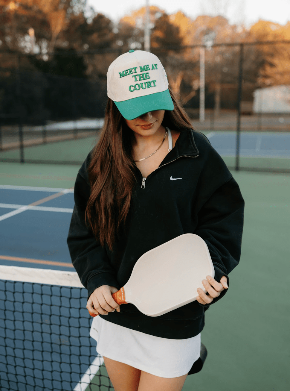 Woman on a tennis court wearing a cap and holding a paddle.