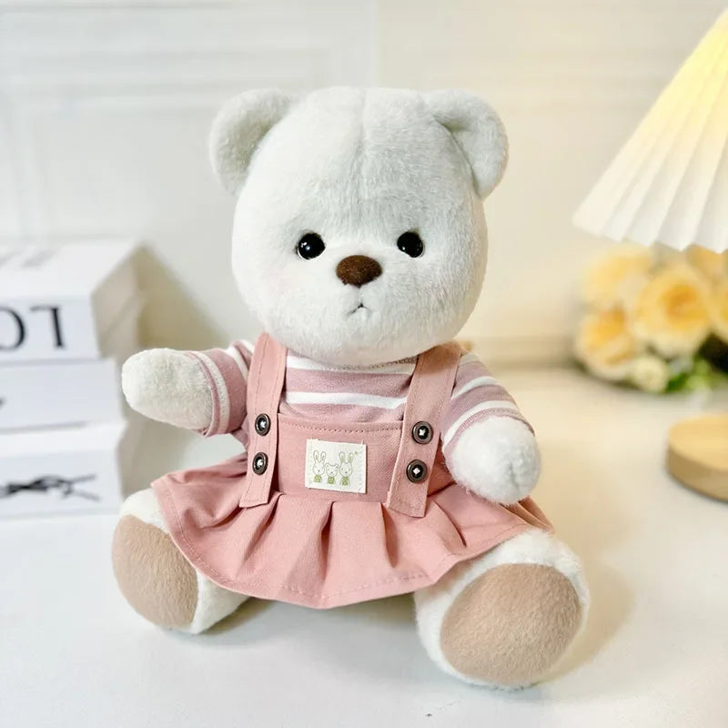 White teddy bear wearing a pink dress with buttons on a light background.