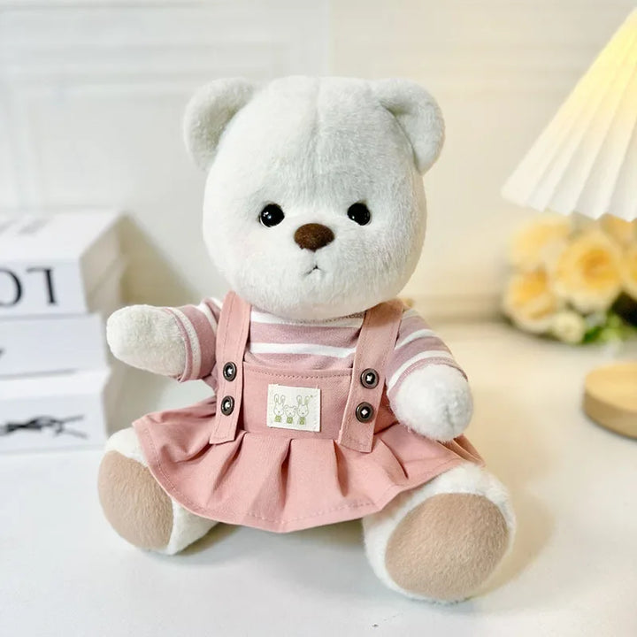 White teddy bear wearing a pink dress with buttons on a light background.