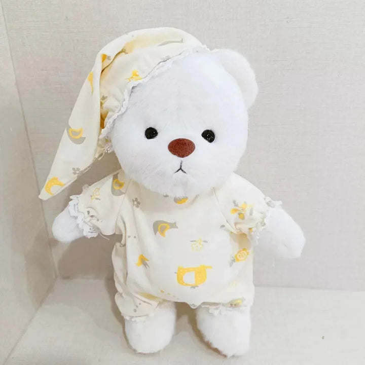 White teddy bear in yellow pajamas with a matching hat on a light gray background.