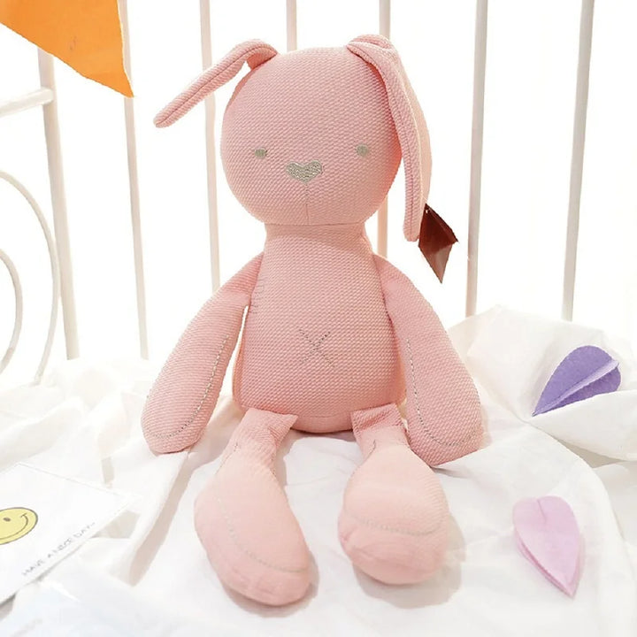 Pink knitted bunny toy on a white surface with a blurred background.