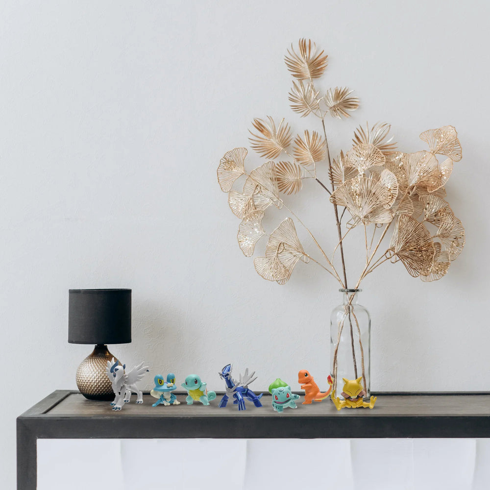 Decorative table with a vase of dried plants, small figurines, and a lamp against a plain wall.