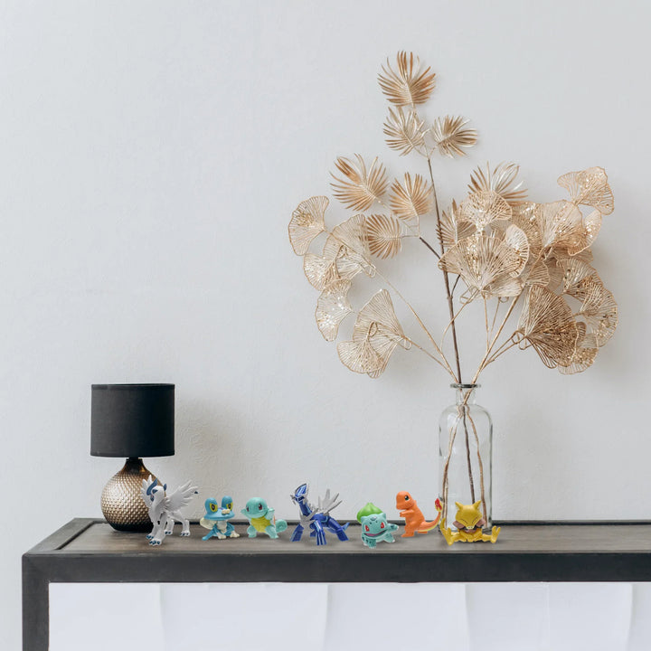 Decorative table with a vase of dried plants, small figurines, and a lamp against a plain wall.