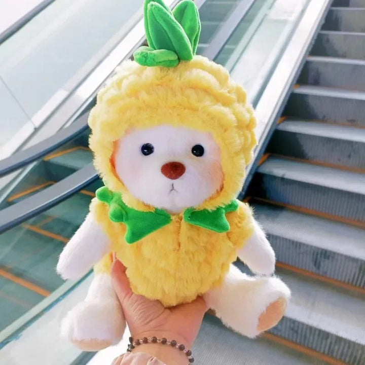 Plush toy bear in a pineapple costume held by a person with an escalator in the background.