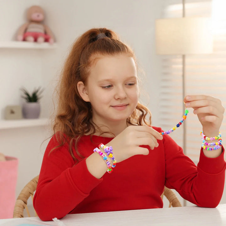 Young girl wearing colorful bracelets, sitting at a table in a bright room.