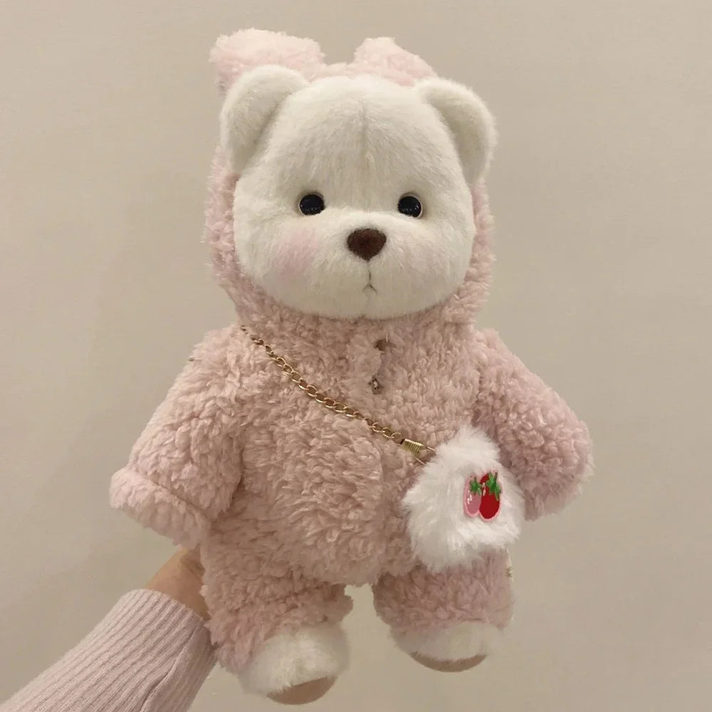 Pink teddy bear with a small bag held by a hand against a neutral background.