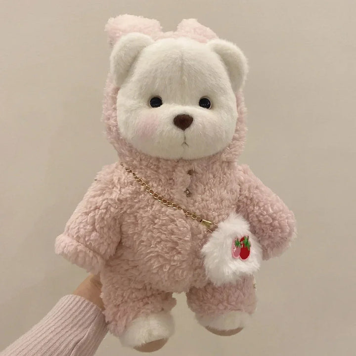 Pink teddy bear with a small bag held by a hand against a neutral background.