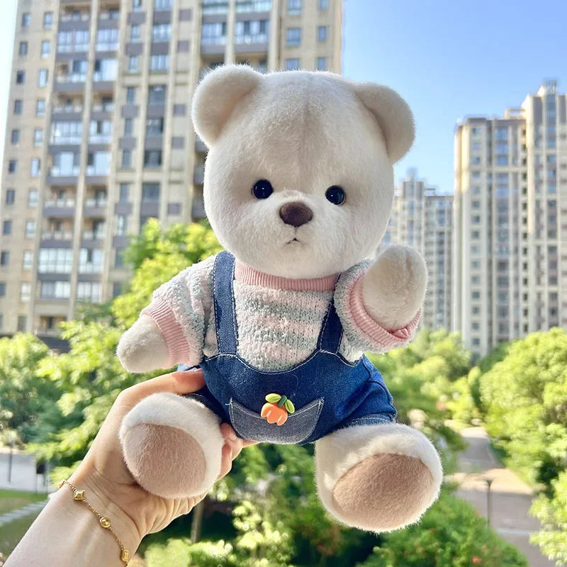 Plush teddy bear in overalls held in front of a cityscape with buildings and greenery.