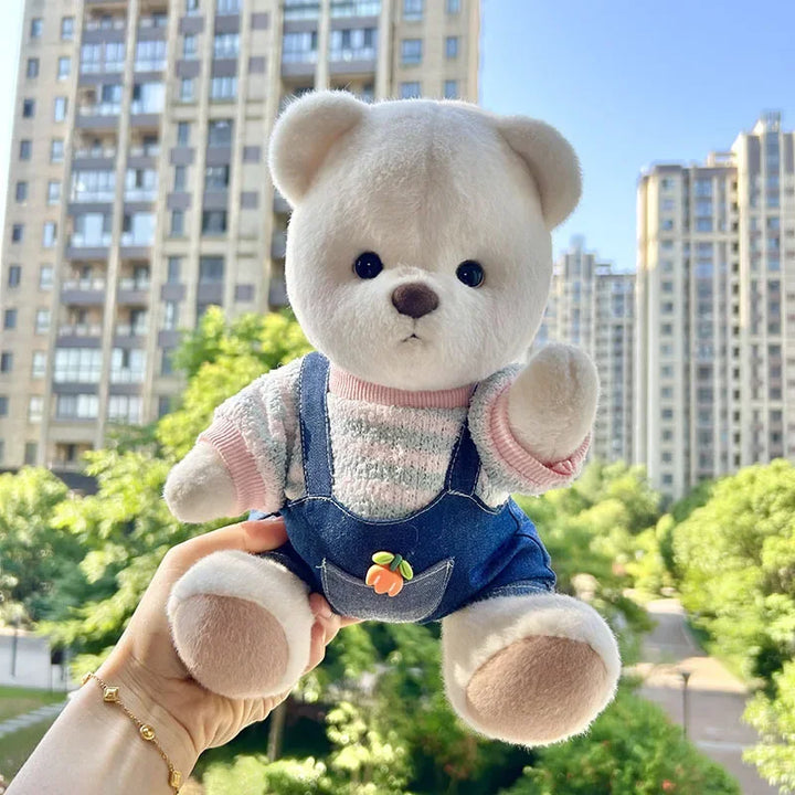 Plush teddy bear in overalls held in front of a cityscape with buildings and greenery.