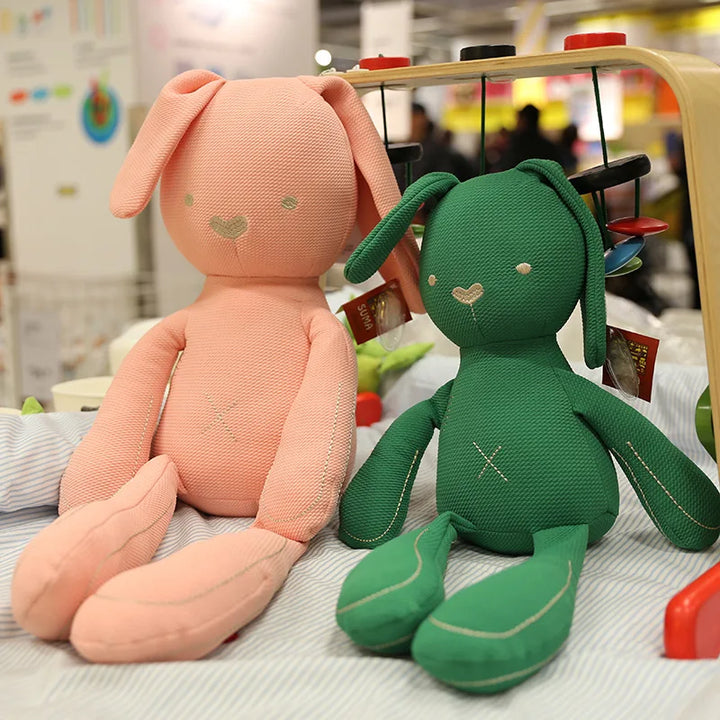 Two plush toys, one pink and one green, sitting on a surface with a blurred background.
