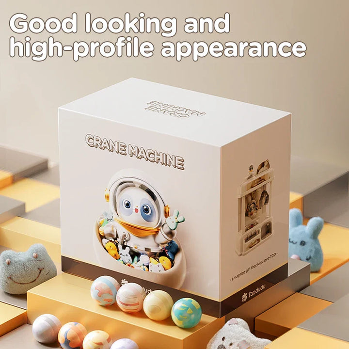 Toy crane machine packaging with cute character and colorful balls on a modern platform.
