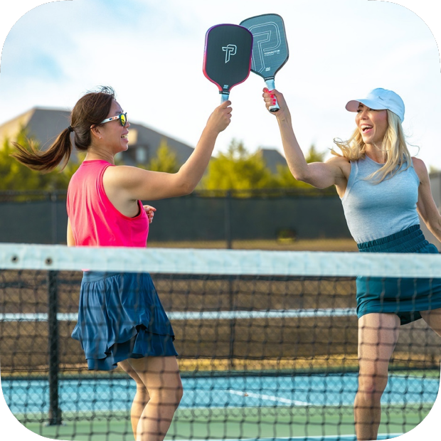Two women on a pickleball court holding paddles above their heads.