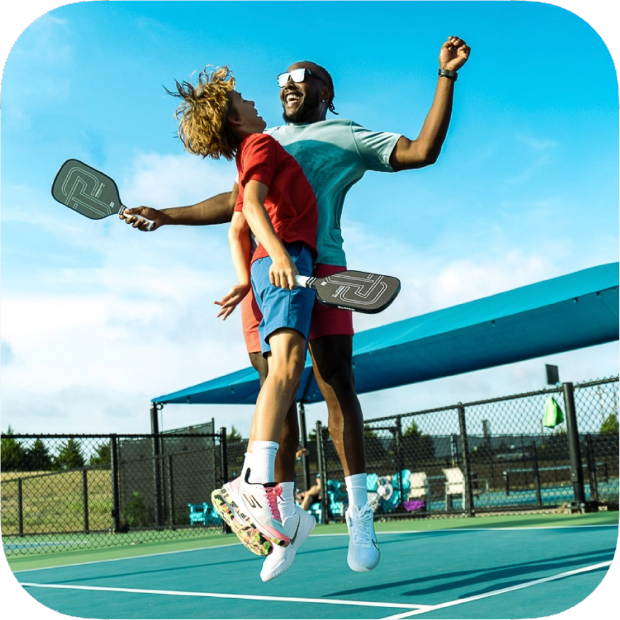 Two people celebrating on a tennis court with paddle sports equipment.