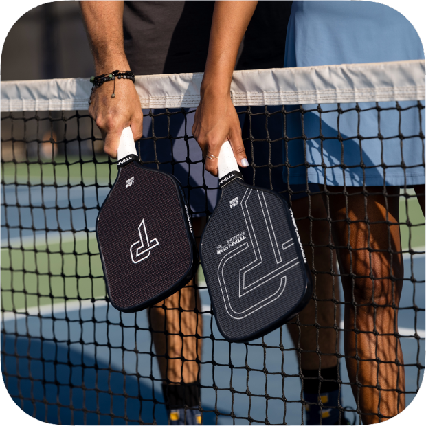 Two pickleball paddles held by a person on a pickleball court.