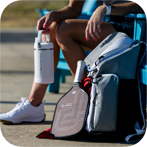 Person sitting with a pickleball paddle and backpack on a bench.