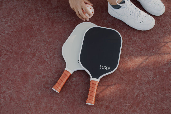 Two pickleball paddles with LUXE branding on a red surface.