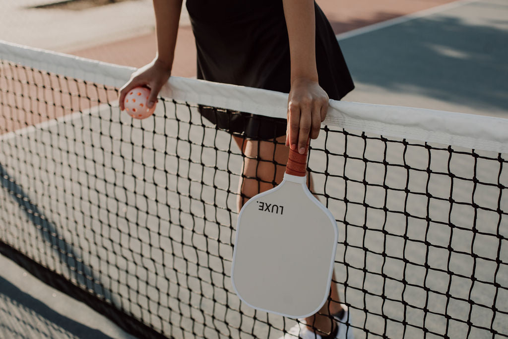 Person holding a pickleball paddle and ball on a court.
