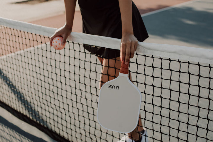Person holding a pickleball paddle and ball on a court.