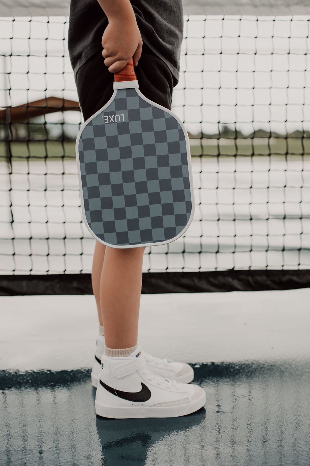 Person holding a checkered pickleball paddle on a court.