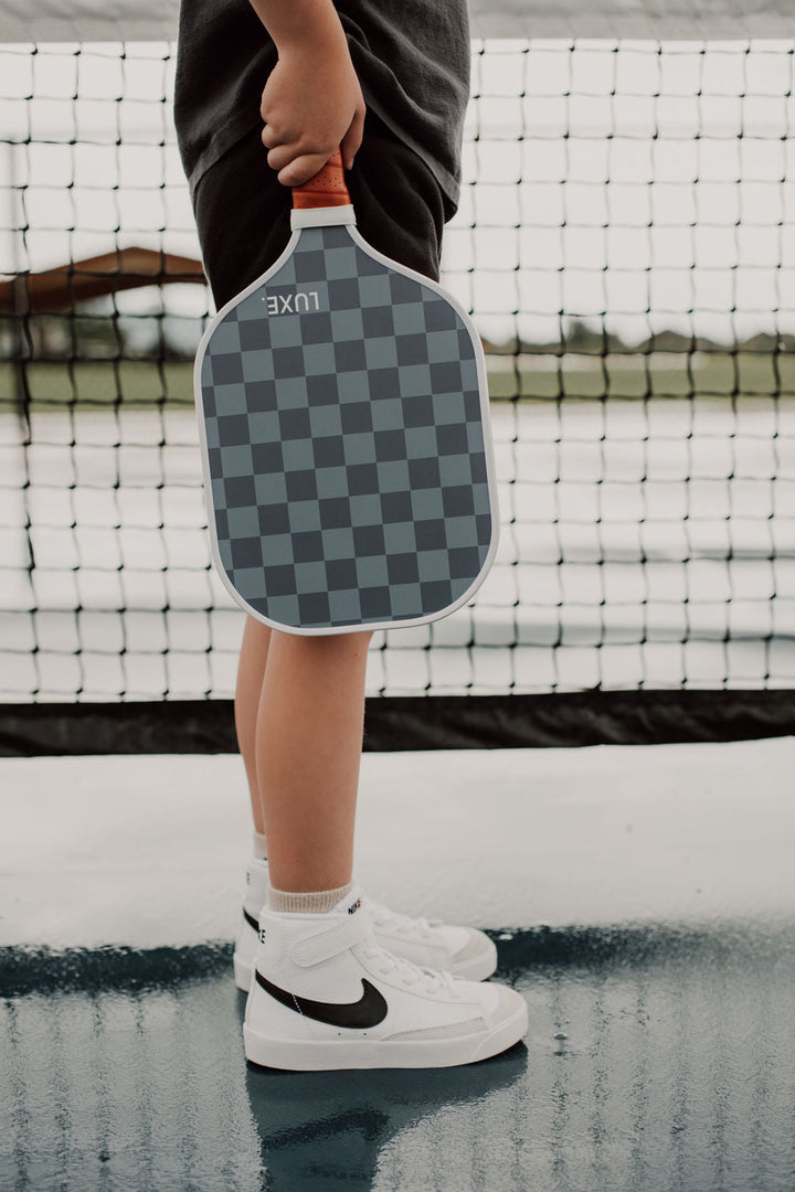 Person holding a checkered pickleball paddle on a court.