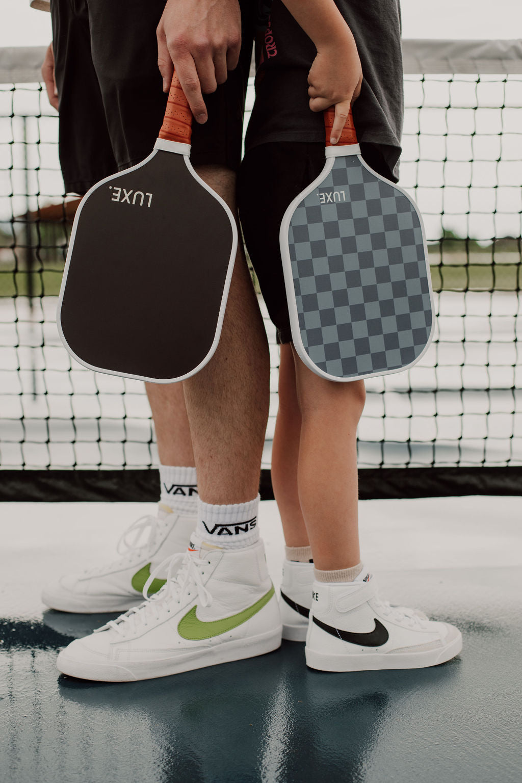 Two people holding pickleball paddles with a netted background.