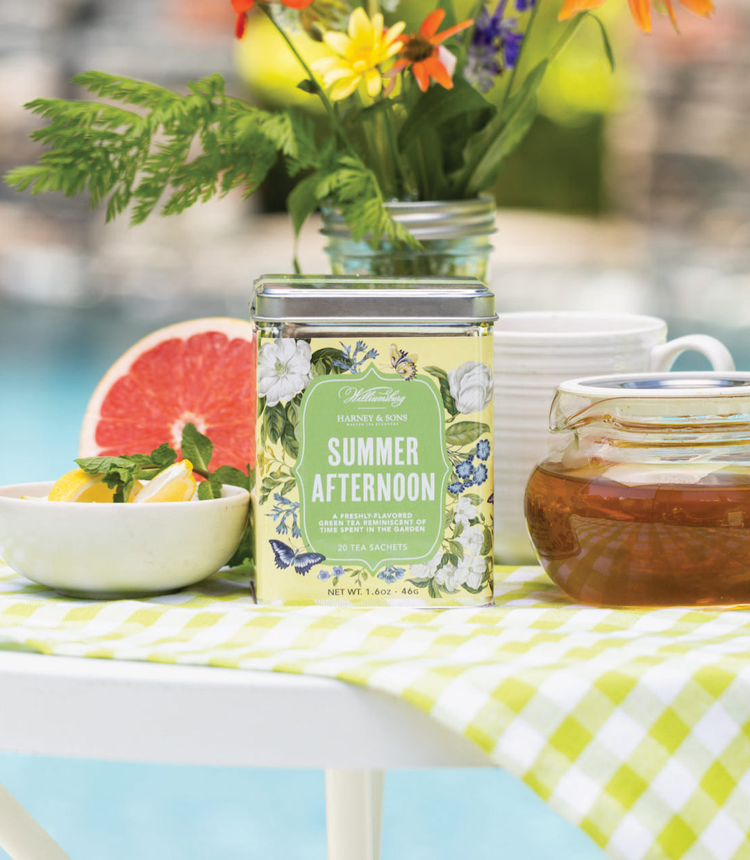 Jar labeled Summer Afternoon on a table with a checkered tablecloth, flowers, and fruit.