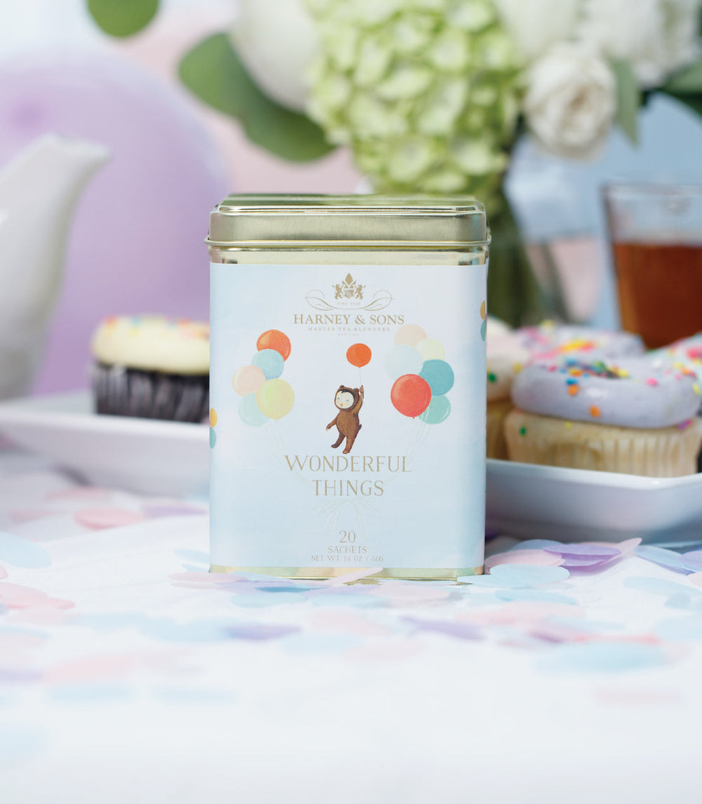 Tea canister with colorful design on a table with cupcakes and flowers