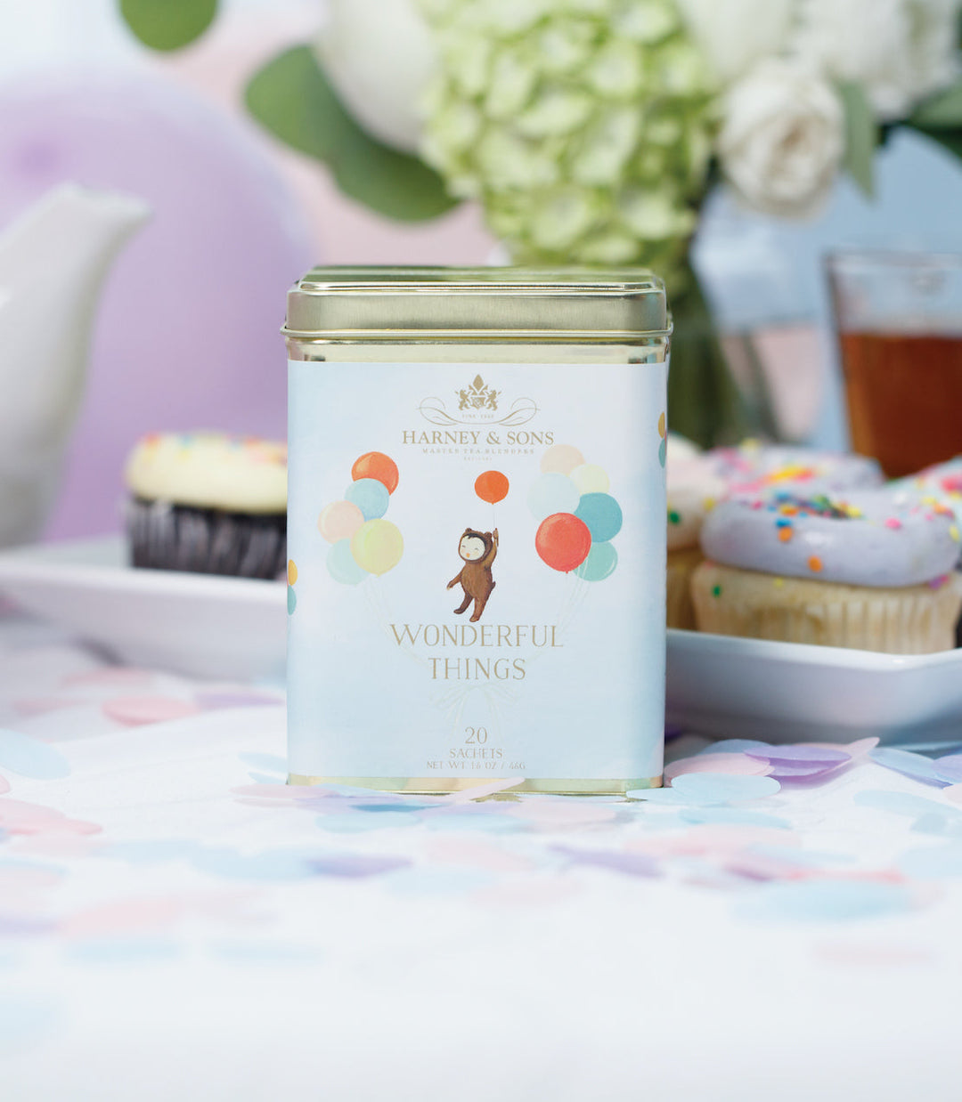 Tea canister with colorful design on a table with cupcakes and flowers