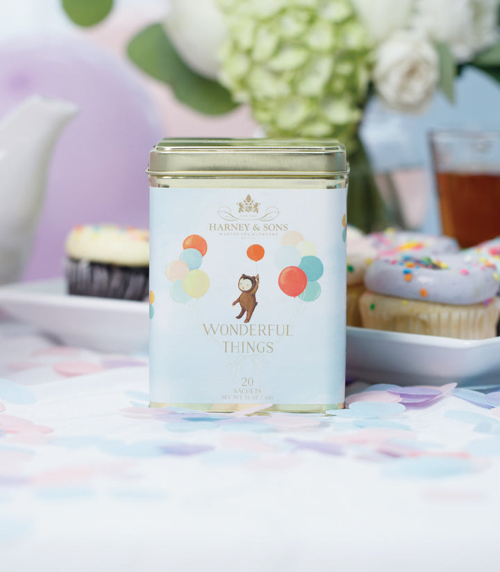 Tea canister with colorful design on a table with cupcakes and flowers