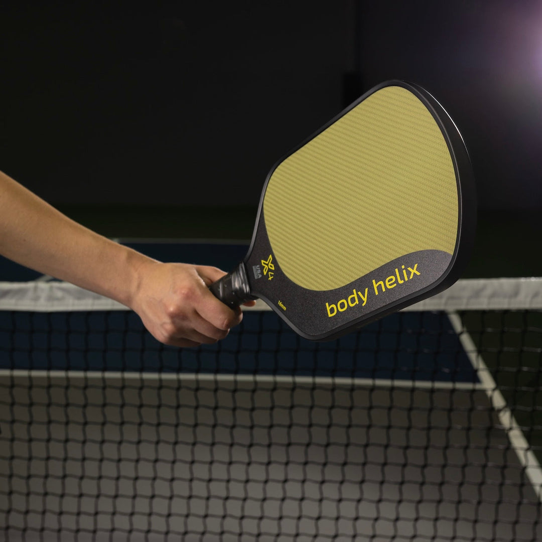 Hand holding a pickleball paddle with body helix branding on a sports court.
