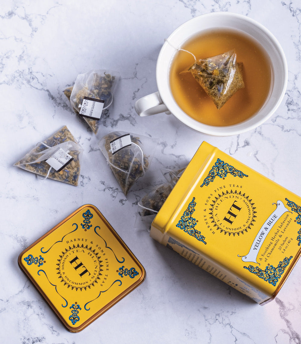 Yellow tea packaging with a cup of tea and tea bags on a marble surface.
